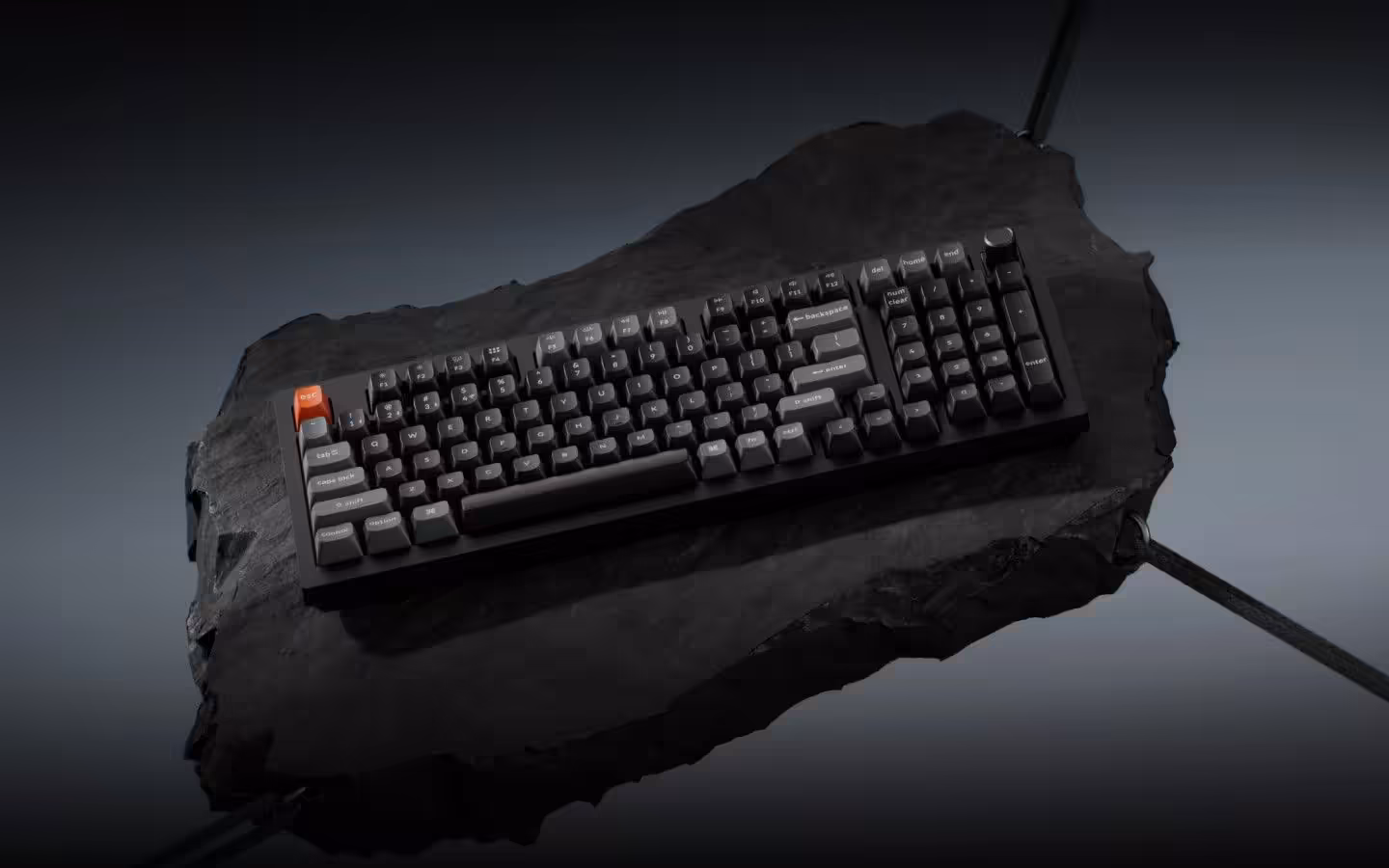 Clavier mécanique Keychron V Ultra 8K sur pierre sombre, touches noires et grises, touche orange distinctive.
