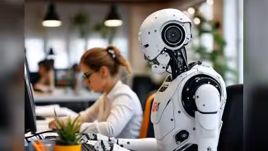 Robot humanoïde assis à un bureau d'ordinateur dans un environnement de bureau moderne.