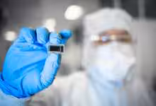 Technicien en blouse blanche et gants tenant un substrat en verre Intel.