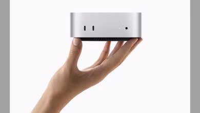 Mac mini argenté tenu dans une main, fond blanc minimaliste