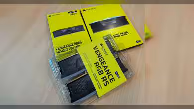 Emballages des kits Corsair Vengeance RGB DDR5 sur table en bois clair.