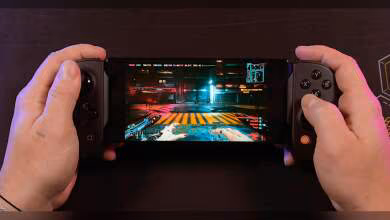 Console portable avec Cyberpunk 2077 écran lumineux fond sombre, mains tenant l'appareil.