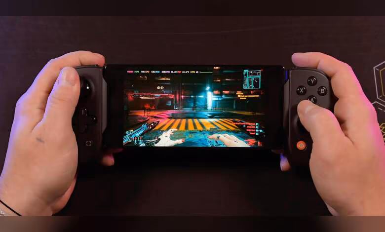 Cyberpunk 2077 tourne sur un Snapdragon 8 Gen 5 via émulation PC, 30 à 50 FPS selon réglages 1 Console portable avec Cyberpunk 2077 écran lumineux fond sombre, mains tenant l'appareil.