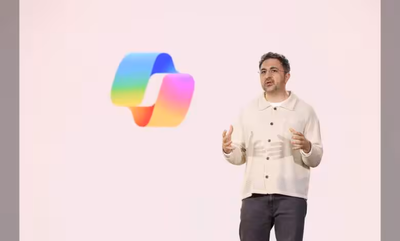Microsoft veut des modèles IA maison pour réduire sa dépendance à OpenAI 1 Conférencier devant un logo coloré en forme de ruban sur fond blanc