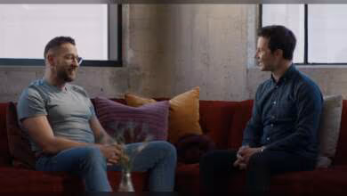 Deux hommes discutant assis sur un canapé rouge dans un environnement de bureau.