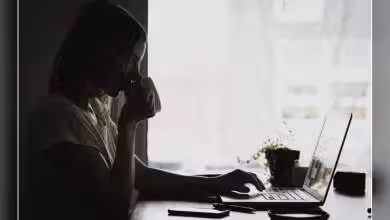 Personne utilisant un ordinateur portable dans une pièce faiblement éclairée, avec plante en arrière-plan.