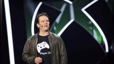 Homme en veste cuir devant logo Xbox, écran LED vert et noir en arrière-plan.