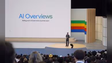 Présentation sur scène avec visuel "AI Overviews" et public attentif, décor aux couleurs de Google.