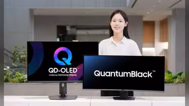 Moniteurs Samsung Display avec logos QD-OLED et QuantumBlack, présentés par une personne dans un hall moderne.