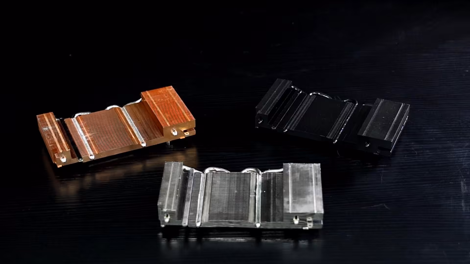 Trois dissipateurs thermiques colorés alignés sur fond sombre net.