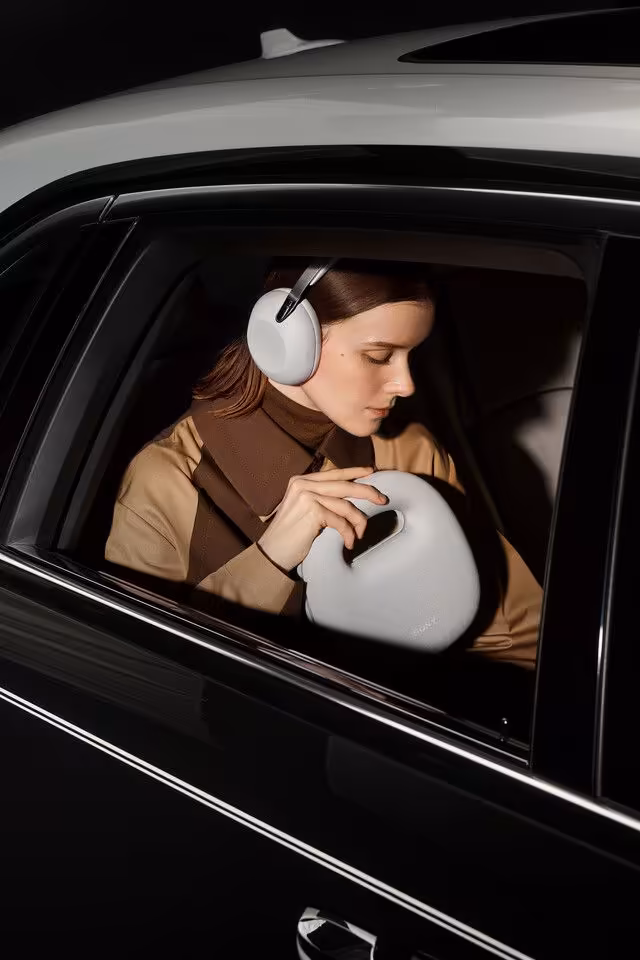 Femme portant un casque Sony blanc, vue depuis une voiture noire, avec sac rond assorti