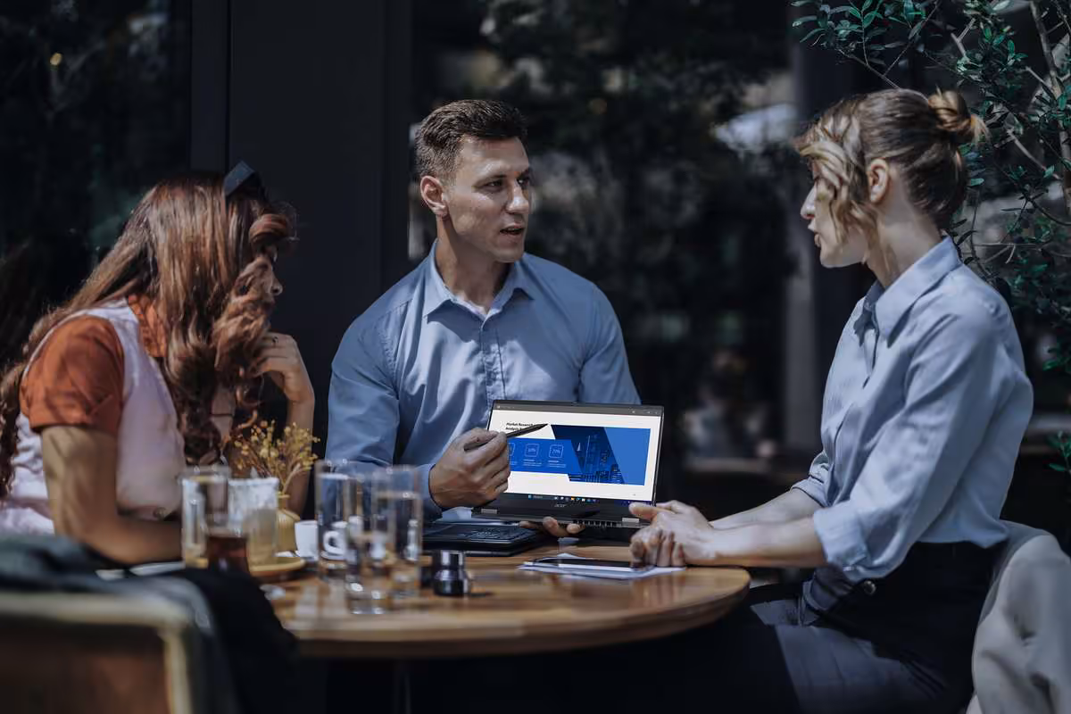 Réunion autour d’une table avec un portable ouvert, écran affichant une interface bureautique.