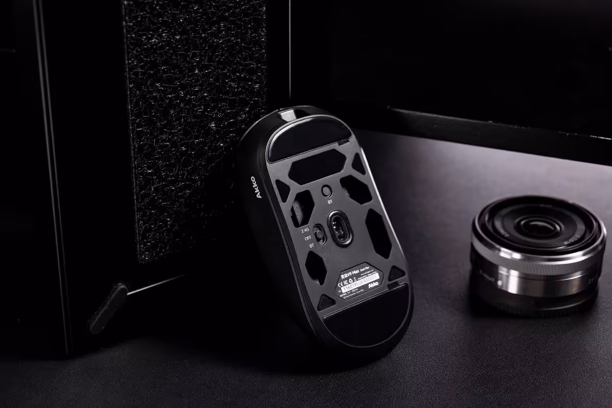Akko Dash Master : une souris gaming de 40 g avec PAW 3955 et polling 8 kHz 2 Dos de la souris gaming Aulac avec coque ajourée et capteur visible, posé près d’un objectif photo