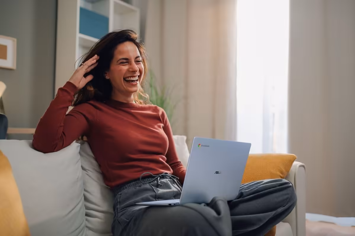 Femme souriante avec un ASUS Chromebook sur ses genoux, assise sur un canapé.