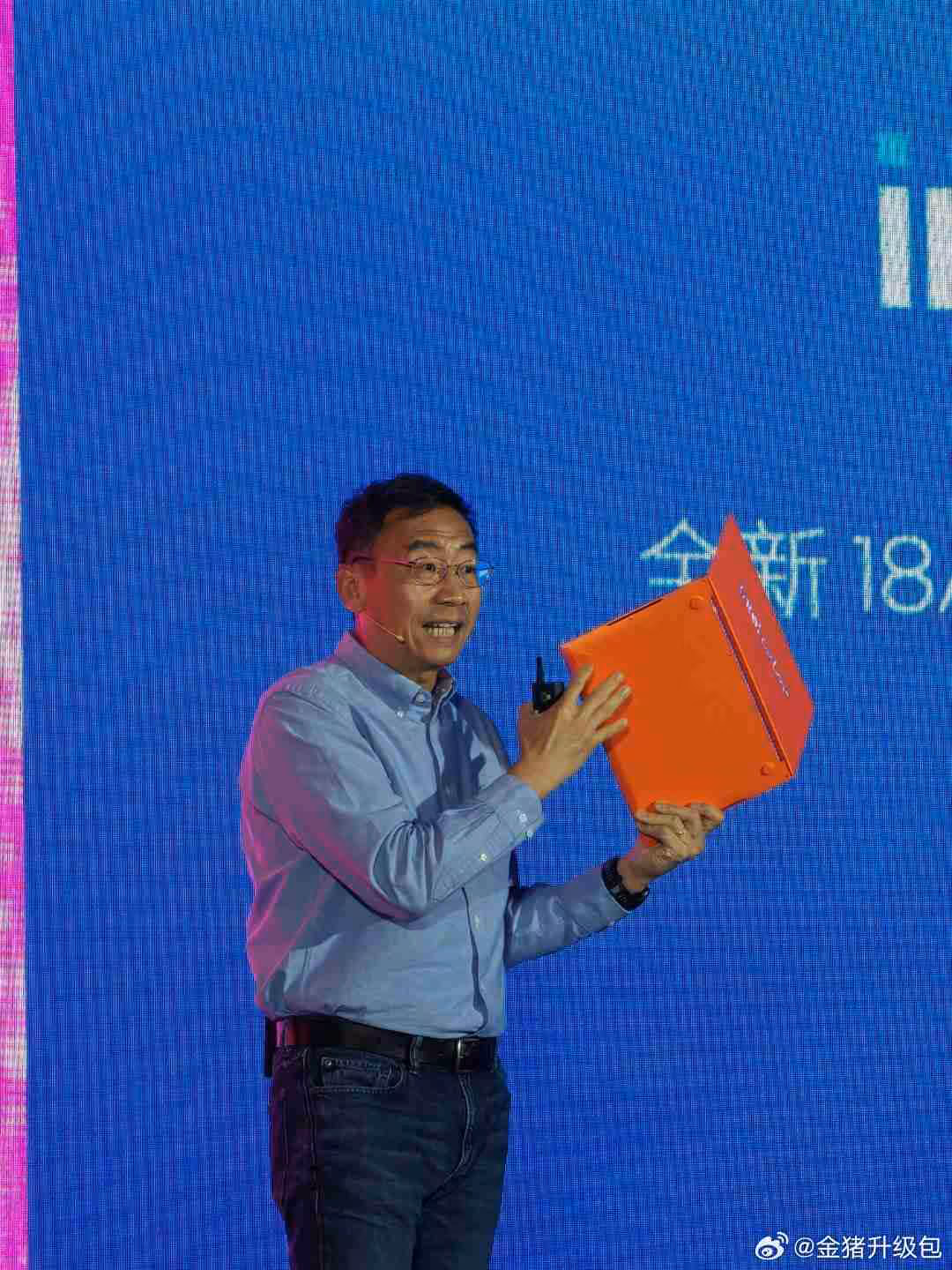 Personne présentant une boîte orange sur scène, fond bleu écrasant.