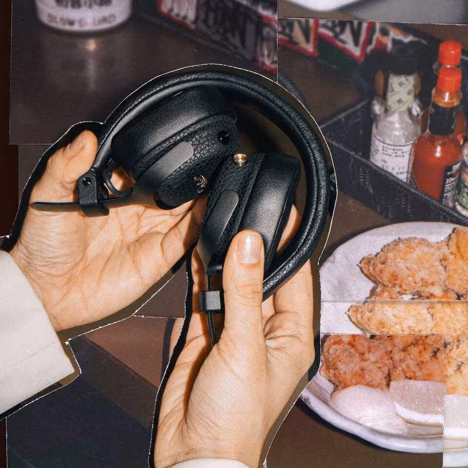 Casque Marshall on-ear plié tenu à la main, avec coussinets noirs, dans un contexte de table.