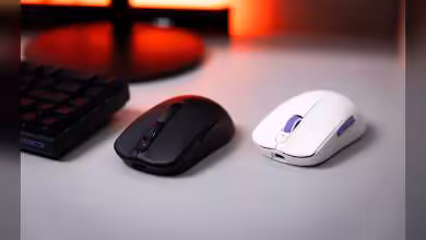 Deux souris gaming sans fil, une noire et une blanche, posées sur un bureau avec clavier en arrière-plan