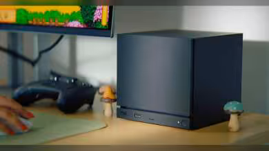 Mini PC noir cubique sur un bureau avec une manette de jeu et décorations champignons.