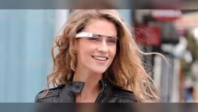 Femme portant lunettes connectées Google Glass, cheveux blonds, veste noire, en extérieur.