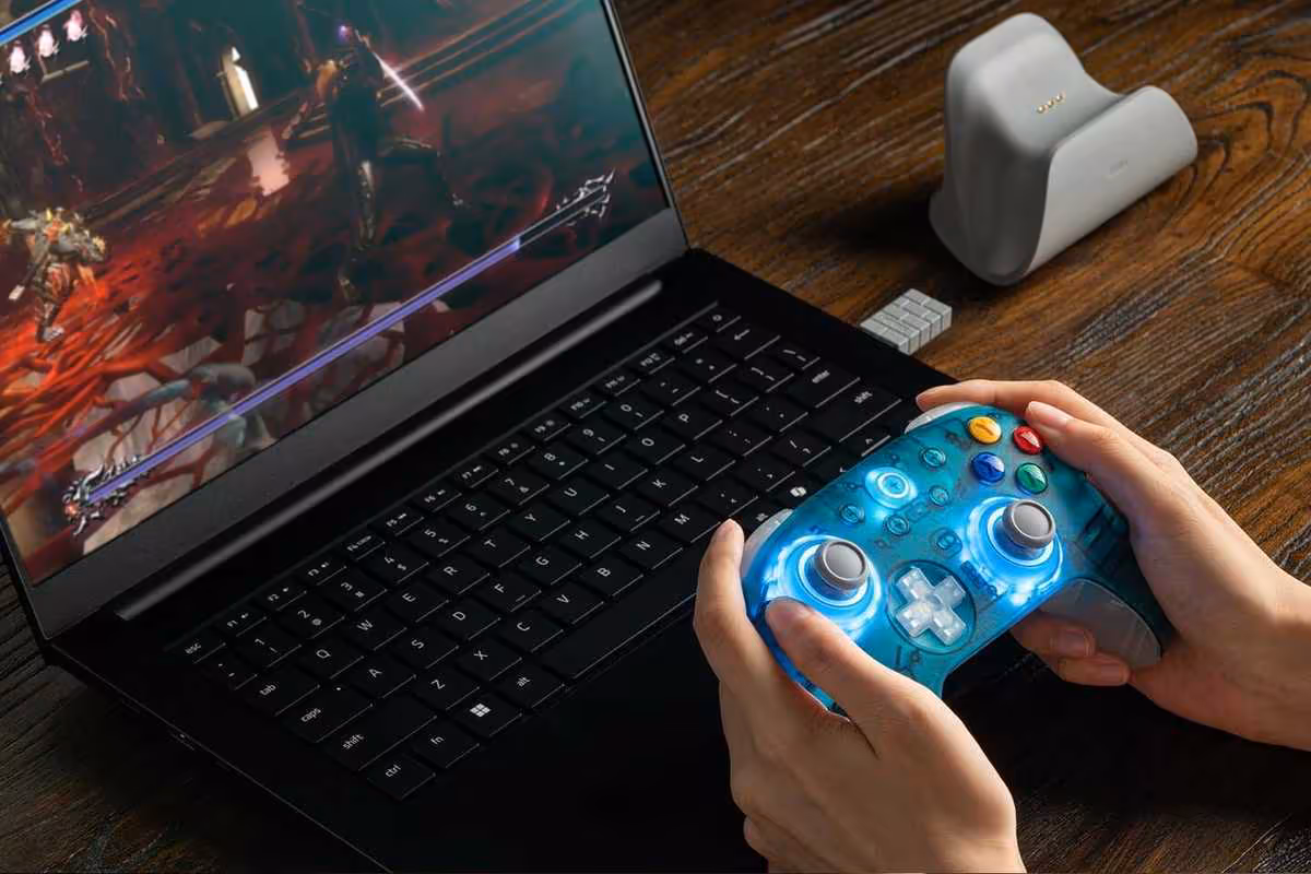 Personne jouant sur ordinateur portable avec manette 8BitDo bleue translucide et dongle USB