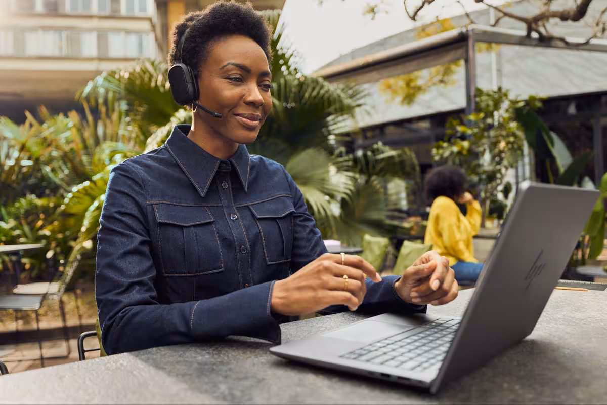 HP Poly déploie un écosystème de collaboration IA unifié à l’InfoComm 2026 3 Femme portant un casque HP Poly travaille sur ordinateur portable dans un espace extérieur verdoyant