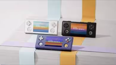 Trois consoles de jeu AYANEO Pocket MICRO 2, différentes couleurs, fond pastel neutre.