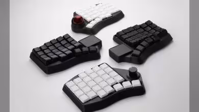 Trois claviers ergonomiques scindés avec keycaps blancs et noirs, trackball rouge et modules séparés