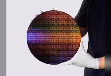 Plaquette de silicium circulaire multicolore tenue par des gants blancs, vue produit sur fond clair