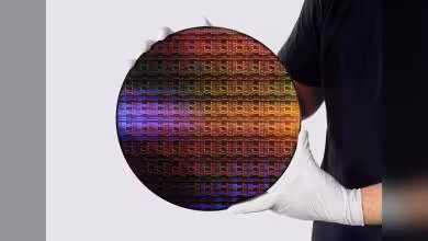 Plaquette de silicium circulaire multicolore tenue par des gants blancs, vue produit sur fond clair