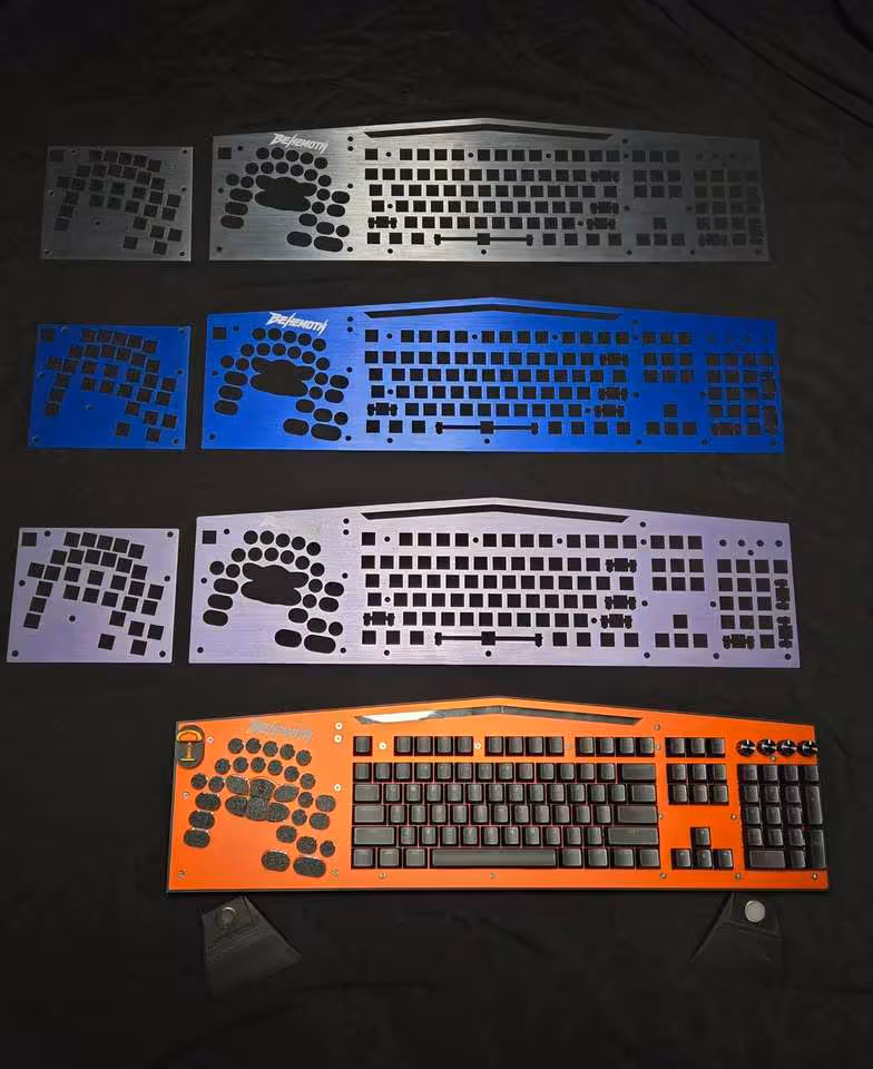 Quatre variantes du clavier Behemoth V2 affichées côte à côte, en noir, bleu, blanc et orange