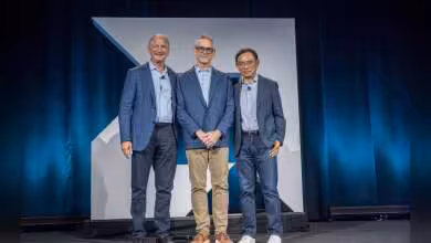 Trois hommes sur scène devant un fond AMD, avec costumes bleus et ambiance conférence tech