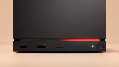 Steam Machine fond beige, LED rouge vif, ports bien visibles.