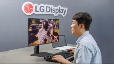 Écran LG Display avec jeu vidéo affiché, utilisateur avec clavier et ordinateur portable à côté.