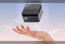 Mini PC GMKtec G5S flottant au-dessus d'une main, fond ciel clair.