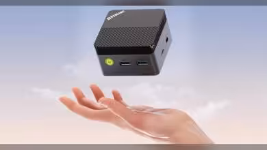 Mini PC GMKtec G5S flottant au-dessus d'une main, fond ciel clair.