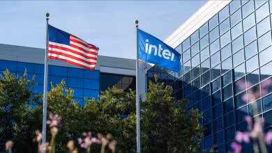 Siège d’Intel avec drapeaux américain et Intel flottant devant une façade vitrée moderne