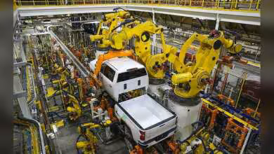 Chaîne d’assemblage automobile avec robots industriels jaunes manipulant une carrosserie et un pick-up blanc en usine