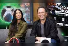 Deux personnes souriantes sur un canapé avec logos Xbox et Microsoft Studios en arrière-plan.