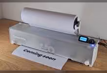 Imprimante OpenPrinter transparente affichant une feuille “coming soon” et un écran de contrôle numérique.