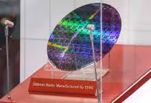 Wafer TSMC de 300 mm exposé sous vitrine, avec reflet arc-en-ciel et support rouge « Manufactured by TSMC »