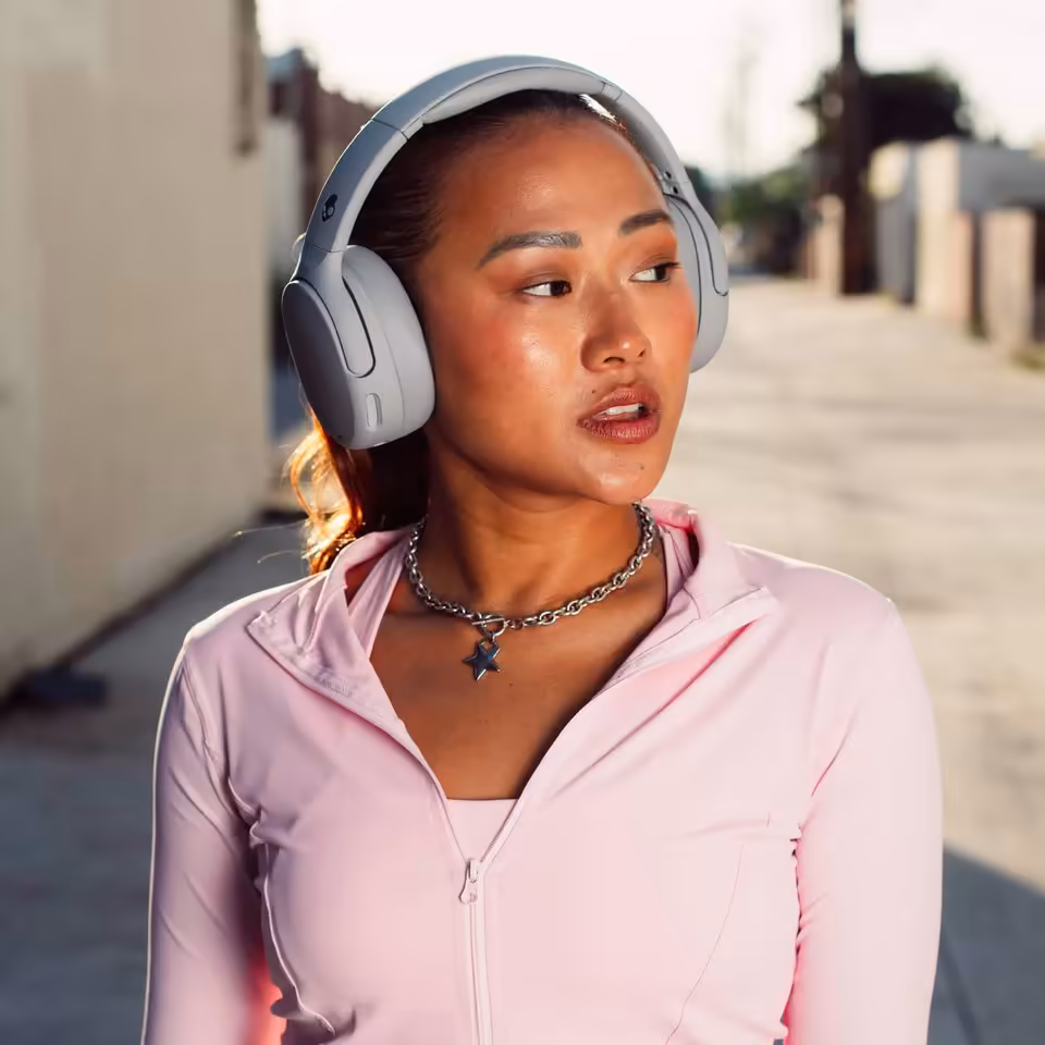 Skullcandy Crusher 720 : THX Spatial Audio, 65 h d’autonomie et basses réglables 4 Femme portant un casque Skullcandy gris clair en extérieur, image lifestyle