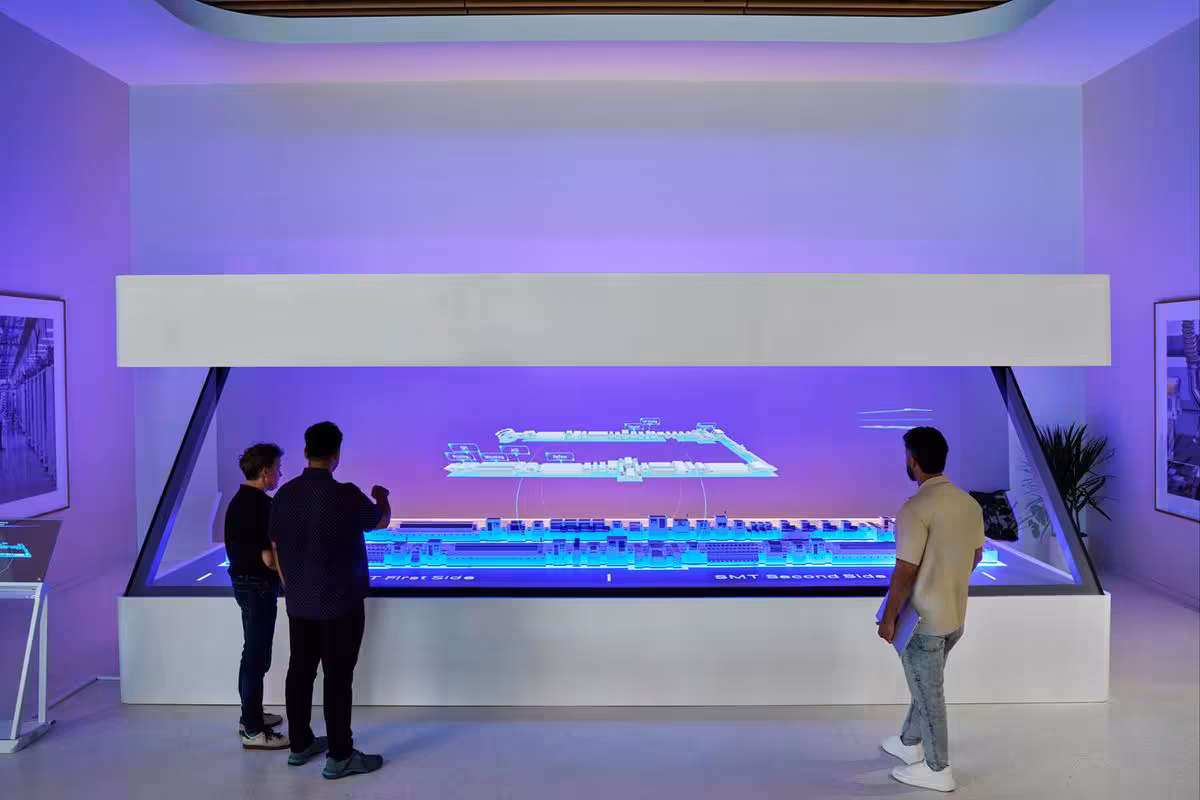 Apple Houston inaugure un centre industriel clé pour l'IA, les PME et le Mac mini 2 Visite d’une salle d’exposition avec maquette interactive rétroéclairée et visiteurs observant une ligne de production.