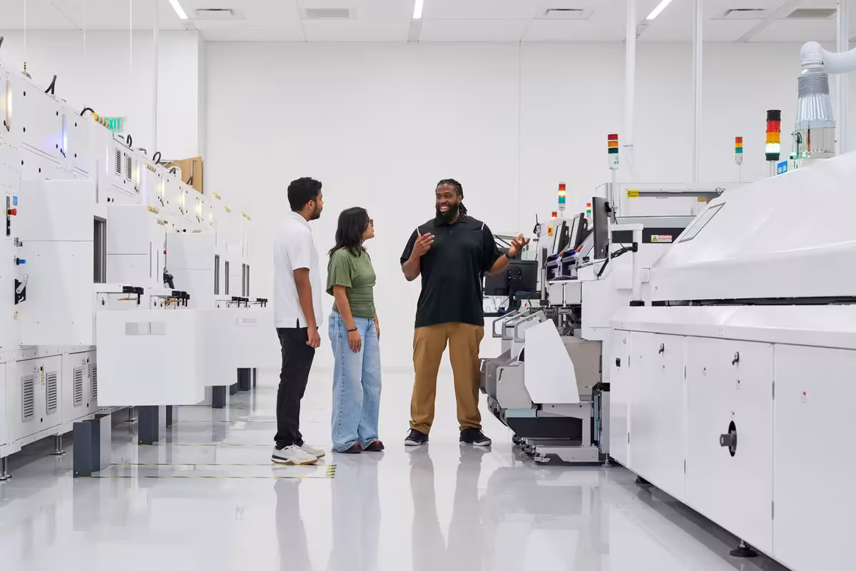 Apple Houston inaugure un centre industriel clé pour l'IA, les PME et le Mac mini 3 Trois personnes dans une usine blanche moderne entourée de machines industrielles de fabrication électronique.
