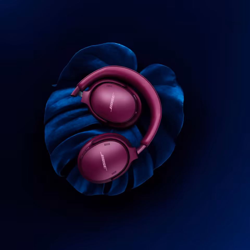 Casque Bose QuietComfort rose, posé sur un coussin bleu sur fond sombre