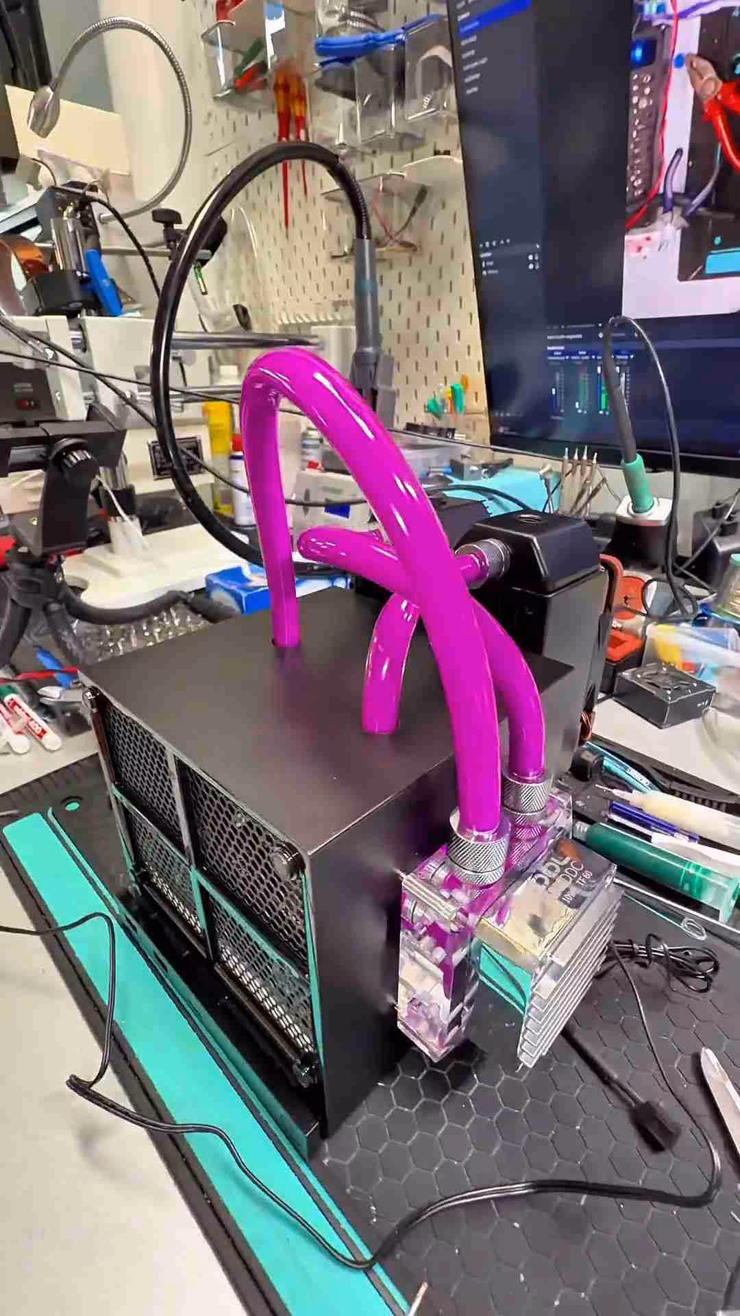 Système water-cooling avec tubes roses sur machine noire, fond atelier, couleurs vives.