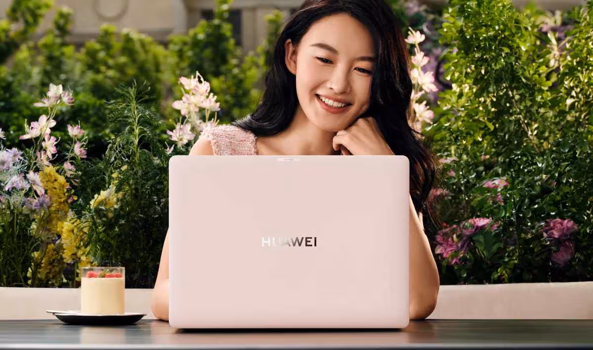 Femme utilisant Huawei MateBook rose en extérieur, environnement fleuri.