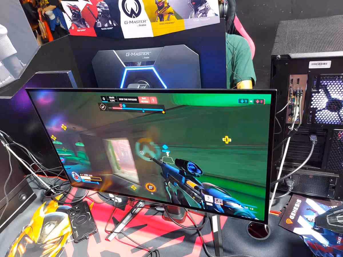 Moniteur iiyama G-Master affichant Overwatch sur stand gaming avec PC et périphériques