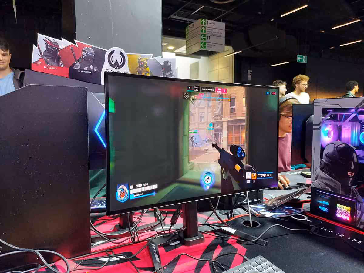 Moniteur gaming iiyama G-Master affichant Overwatch, vu sur un stand avec tour PC RGB