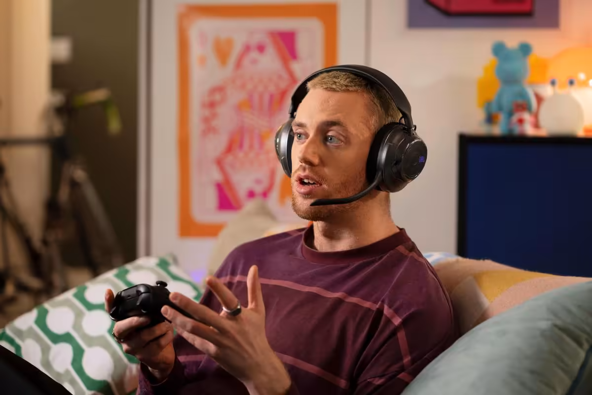 JBL Quantum 520 : la gamme gaming s’élargit avec les 520X et 120 dévoilés à la Gamescom 2026 7 Homme portant un casque gaming JBL noir et jouant à la manette dans un salon.