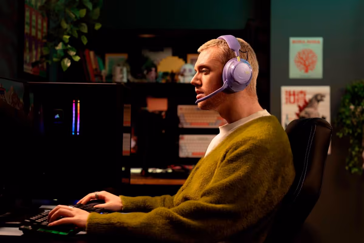 JBL Quantum 850 : un casque gaming premium à 279,99 € avec ANC et head tracking 3 Homme jouant au PC avec casque JBL Quantum violet et micro intégré dans une pièce sombre